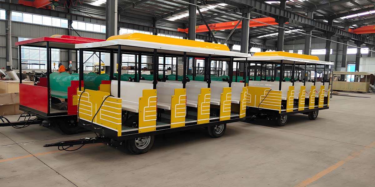 Colorful open-sided trackless train with yellow and red details, shown in a factory setting, designed for easy passenger boarding and sightseeing.