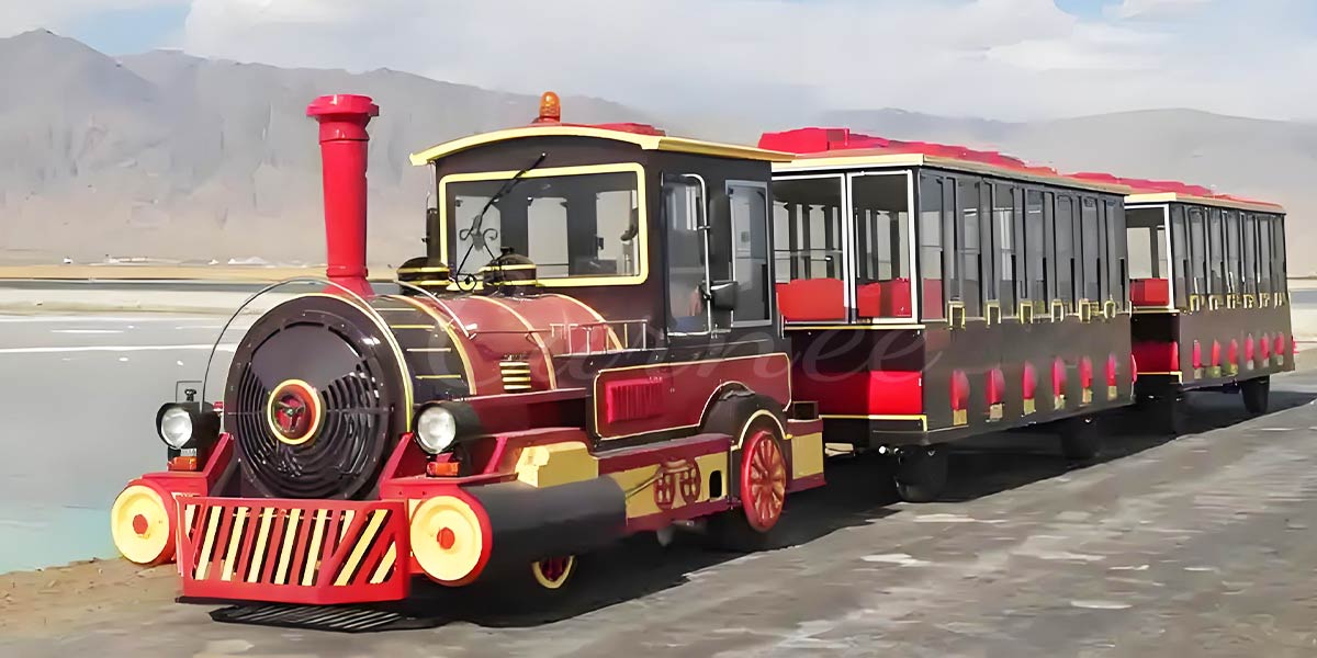 Classic red and gold retro-style trackless train with enclosed carriages, traveling outdoors with scenic mountains in the background.