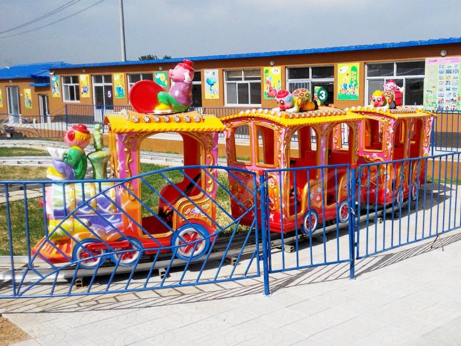 Brightly colored clown train ride at an amusement park, designed for children's enjoyment
