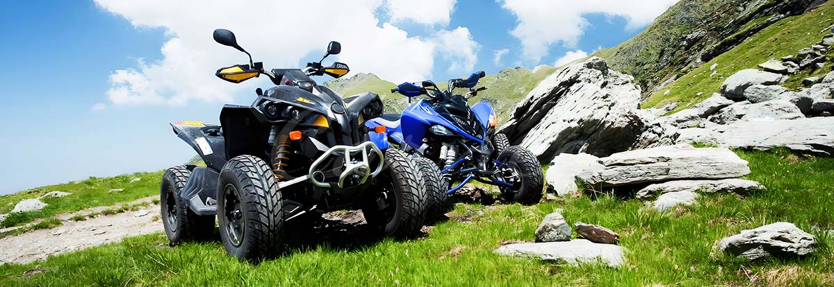 ATV parked on rocky terrain with a scenic mountain background, showcasing the vehicle's capability for adventure and off-road exploration.