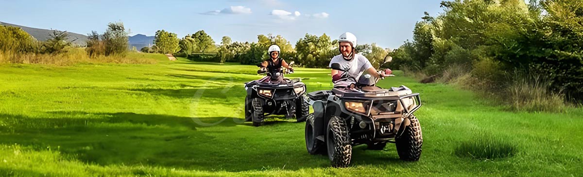 Two people riding ATVs on a lush green field, highlighting the versatility and fun of recreational ATV riding.