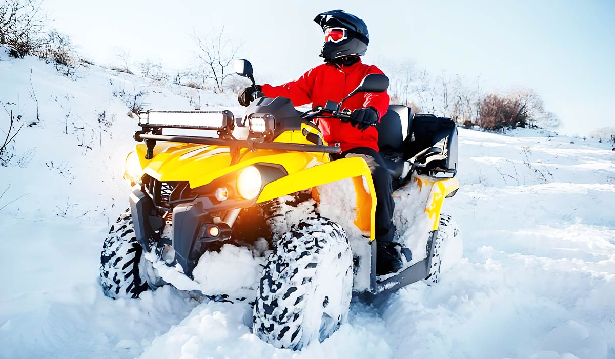 A person riding a yellow ATV through snow-covered terrain, enjoying winter adventures.