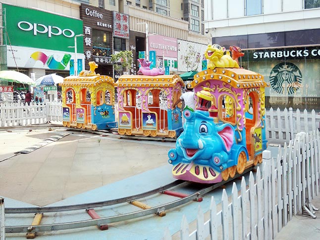 Children enjoying a joyful ride on the colorful elephant-themed track train at a shopping mall