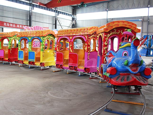Bright and colorful elephant track train for kids at a fun fair, featuring multiple carriages.
