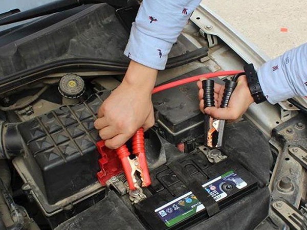 Hands checking and connecting battery cables to ensure safe operation of amusement park train rides.