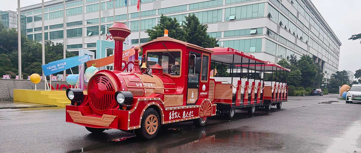 Large red trackless amusement park train ride operating outdoors with safety features.